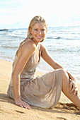 A blonde woman by the sea wearing a beige summer dress