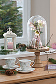 Small bouquet with snow roses HCG 'Maestro' under a glass bell jar, mugs, lantern, pine branches, and pinecones