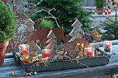 Forest motif on a zinc tray: small wooden fir trees, rust moose silouettes, pinecones, lanterns, leaves, and moss