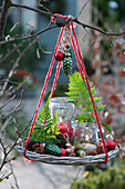 Hängende Weihnachtsdekoration mit Windlichtern, Farnblättern, Christbaumschmuck und Zapfen