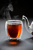 Dampfender schwarzer Tee in Glasbecher