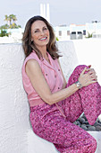 A long-haired woman wearing a pink sleeveless blouse and summer trousers