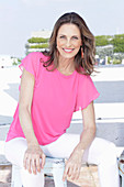 A long-haired woman wearing a pink summer top and white trousers