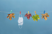 Gesichtsmaske hängt an Wäscheleine mit Herbstlaub