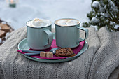 Tassen mit heißem Cappuccino auf Teller mit Zucker, Keks und Kaffeelöffeln