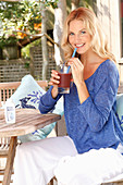 A blonde woman wearing a blue shirt and white trousers with a drink