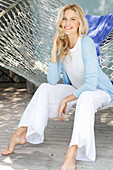 A blonde woman wearing a white top and a light blue cardigan sitting in a hammock