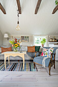 Armchair, coffee table with bouquet of flowers and sofa in living room with white-painted wooden ceiling