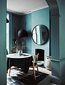 Blick durch Rundbogen-Ausschnitt auf rundne Tisch mit Stühlen in petrolfarbenem Zimmer