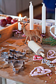 Wooden board with candles, deer figure, rolling pin, gingerbread, and cookie cutters