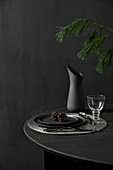 Schwarzer, gedeckter Tisch mit Lärchenzweig vor schwarzer Wand