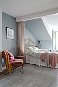 View of double bed with rattan headboard behind a curtain, armchair in the foreground