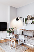 Sand-coloured sofa, wall-mounted lamp and tray table with vases of white flowers