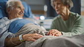 Wife visiting elderly man on hospital ward