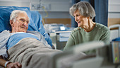 Wife visiting elderly man on hospital ward