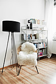 Black standard lamp and easy chair with sheepskin rug in front of shelves
