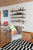 Armchair on black and white striped carpet in open living room, wall shelf in the background