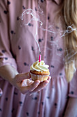 Woman in a pink dress holding a cupcake with a pink candle and smoke coming out from it