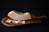 A piece and a thin slice of lardo on a wooden board