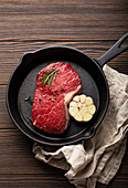Raw beef steak with seasonings, garlic and rosemary in frying pan