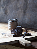 Schokoladenstücke auf Holzschneidebrett mit Messer und Zinnbecher