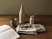 Still-life arrangement of stoneware bottle, vase, fabric and book
