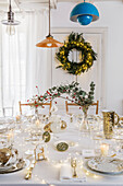 Christmas table set in white, in the background door wreath with string lights