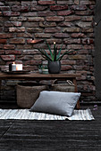 Wooden bench with plant and candle, wicker basket, rug and cushion on terrace
