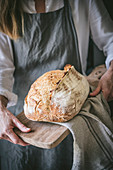 Woman holds homemade sourdough bread on wooden board