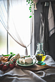 Stilleben mit Mozzarella, Tomaten und Olivenöl auf Tisch am Fenster
