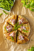 Homemade whole wheat pizza with tzatziki sauce, green peas, cheese and prosciutto