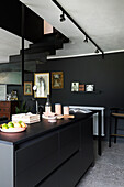 Schwarze Kücheninsel in offenem Wohnraum mit schwarzer Wand, Treppe zur Galerie