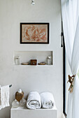Rolled towel and glass vases on a cupboard, above is a wall niche with decorative objects and picture in bathroom