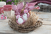 Ungewöhnliches Osternest aus Clematisranken und Heu, mit Ostereiern in Servietten gebunden, dekoriert mit Blüten von Tausendschön