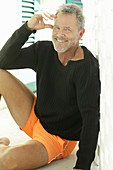 A grey-haired man wearing a black jumper and orange shorts