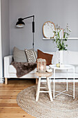 Weißes Sofa mit Kisssen, weißer Beisteltisch mit Krugvase und Holzhocker mit Laterne im Wohnzimmer