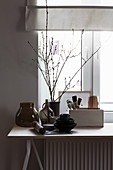 Crockery, glass vessels and branches on table below window