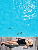 Frau im Badeanzug am Poolrand liegend, Gesicht mit Strohhut verdeckt