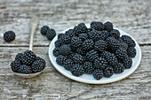 Blackberries in plate and spoon on grey wood deck