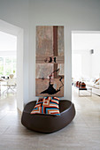 Designer pouffe with patterned scatter cushion below modern artwork on wall