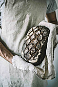 Bäcker hält Sauerteigbrot mit Hanfsamen in den Händen