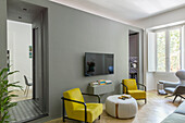 Gelbe Sessel, Couchtisch, Konsole und Fernseher an grauer Wand