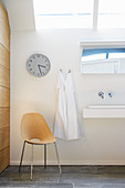 Chair below wall clock in white bathroom with skylight