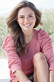 A young, long-haired woman wearing a pink blouse and shorts sitting in the sand