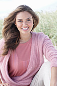 A young, long-haired woman wearing a pink blouse and a pink wrap-around jumper