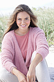 Langhaarige junge Frau in rosa Bluse und rosa Wickelpullover