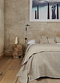 Doppelbett und Baumstammhocker im Schlafzimmer mit sandfarbenen Wänden