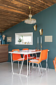 Orange dining area in front of blue-grey wall in open-plan living room with rustic wooden ceiling