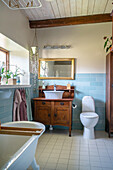Freestanding bathtub, antique washstand and toilet in bathroom with light blue wall tiles