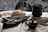 Black crockery, black napkins and bread on a beige linen tablecloth